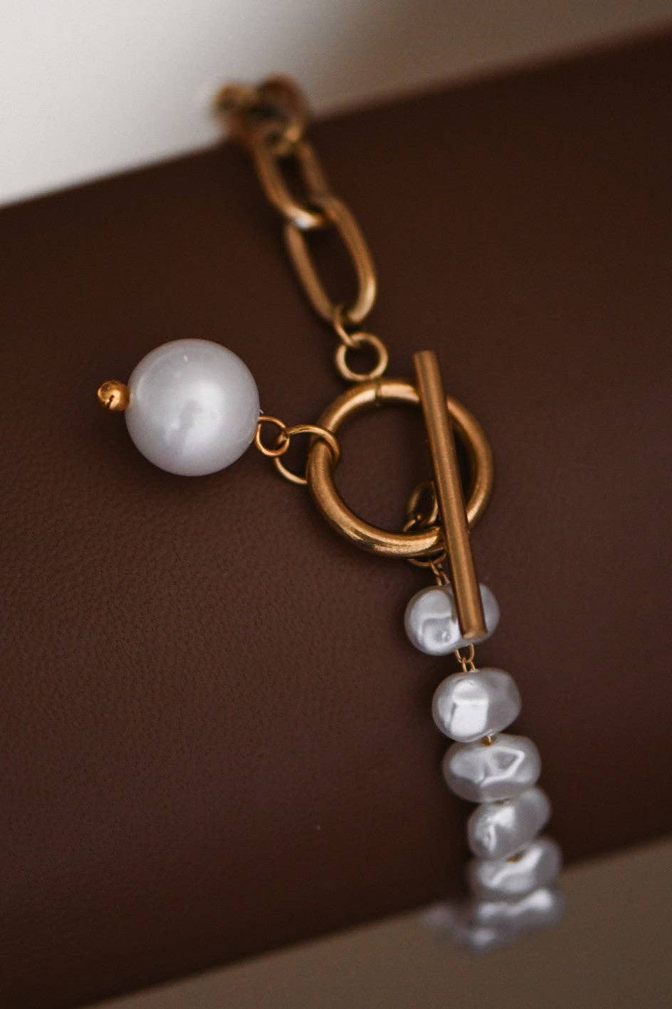 Gold bracelet with a pearl charm on a brown background