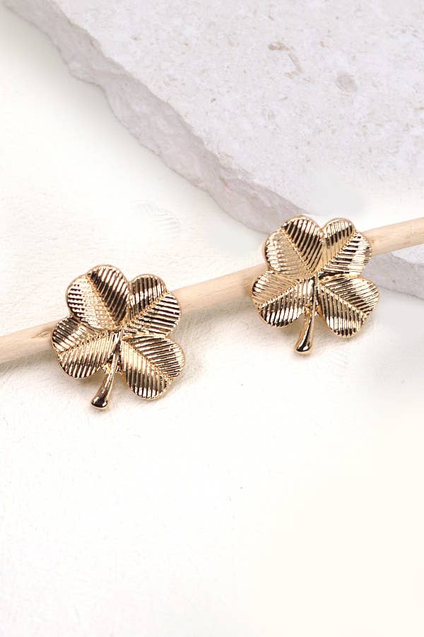 Two gold, four leaf clover shaped stud earrings on a white stone background