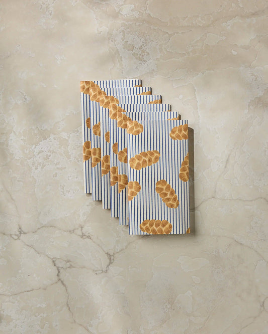 A stack of paper napkins with a pattern of golden-brown bread loaves on a white background with thin blue vertical stripes, displayed on a beige marble surface.