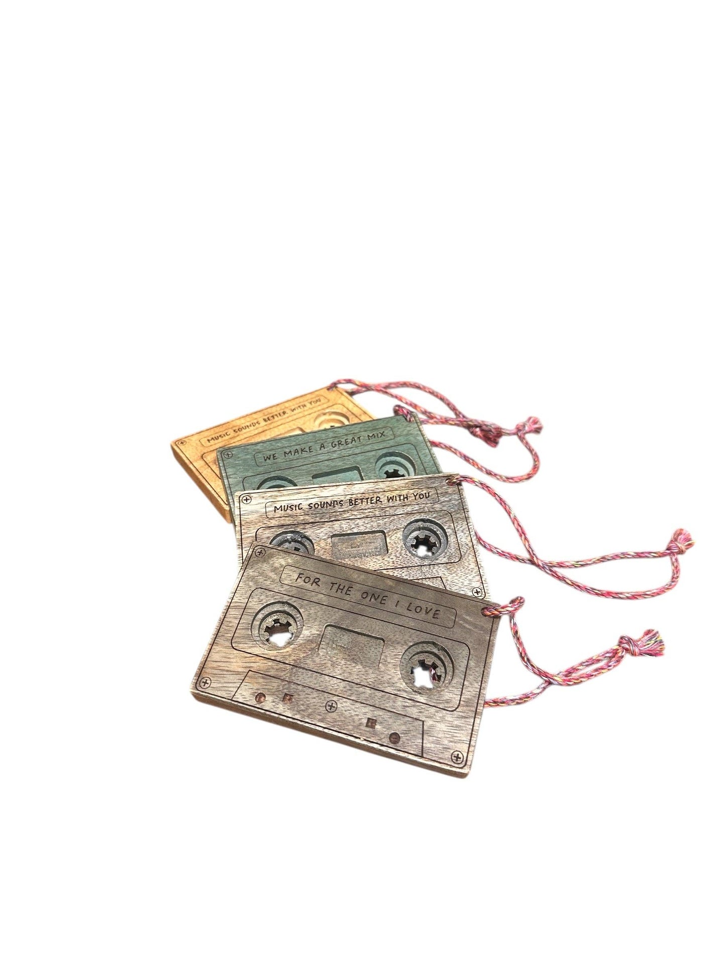 Three vintage cassette tape-shaped ornaments or charms in muted green, beige, and gray, each with a pink drawstring cord, arranged on a plain white background.