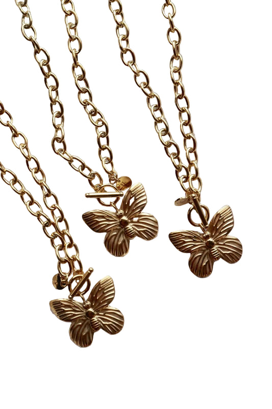 Three gold butterfly necklaces on a textured white surface