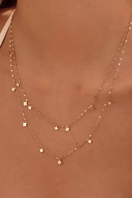gold necklace with small square pendants on a person's neck against a neutral background