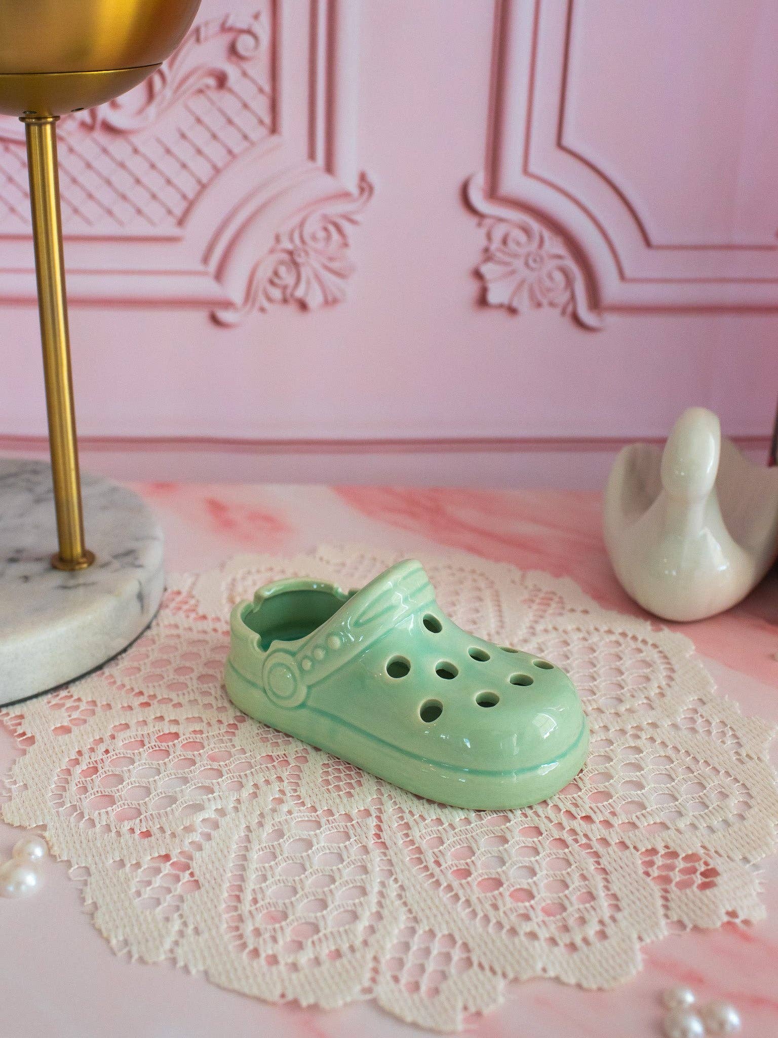 Mint green clog tray on a lace doily with a decorative pink wall in the background