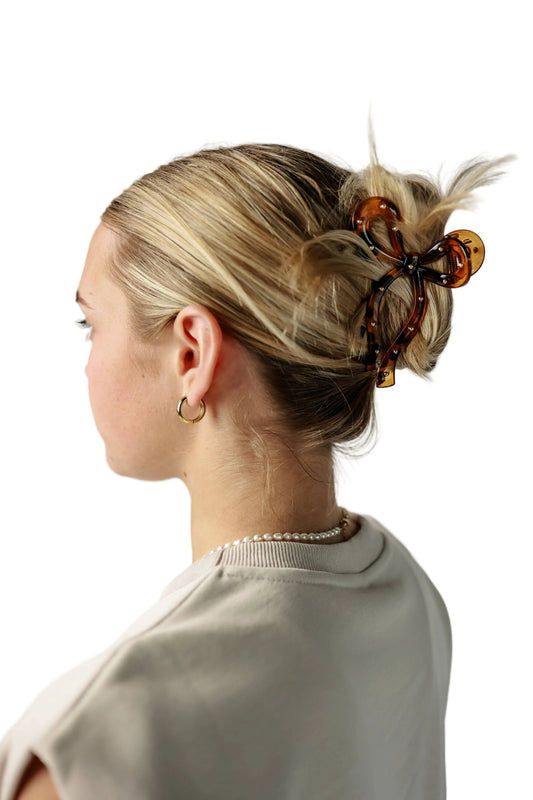 Person with styled hair using tortoiseshell hair clips against a plain background