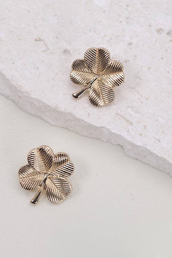Two gold, four leaf clover shaped stud earrings on a white stone background