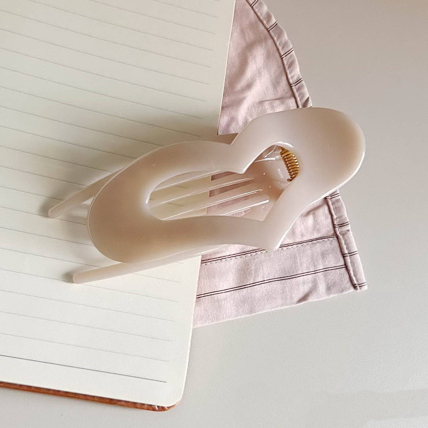 Off-White, heart shaped "lay-flat" claw clip on an open notebook
