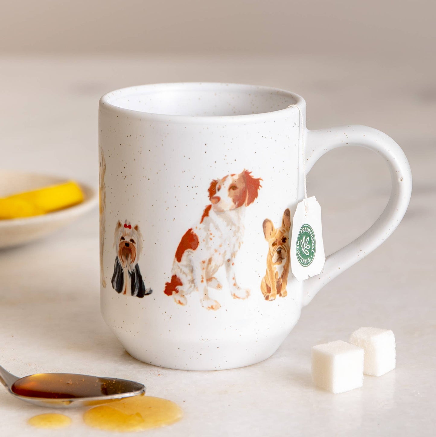 White mug with dog illustrations on a table with tea and sugar cubes.