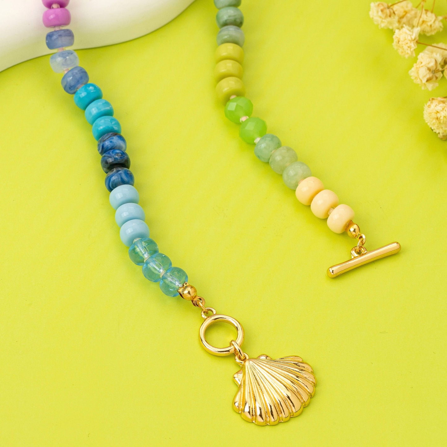 Necklace with colorful beads and a gold shell charm on a yellow background