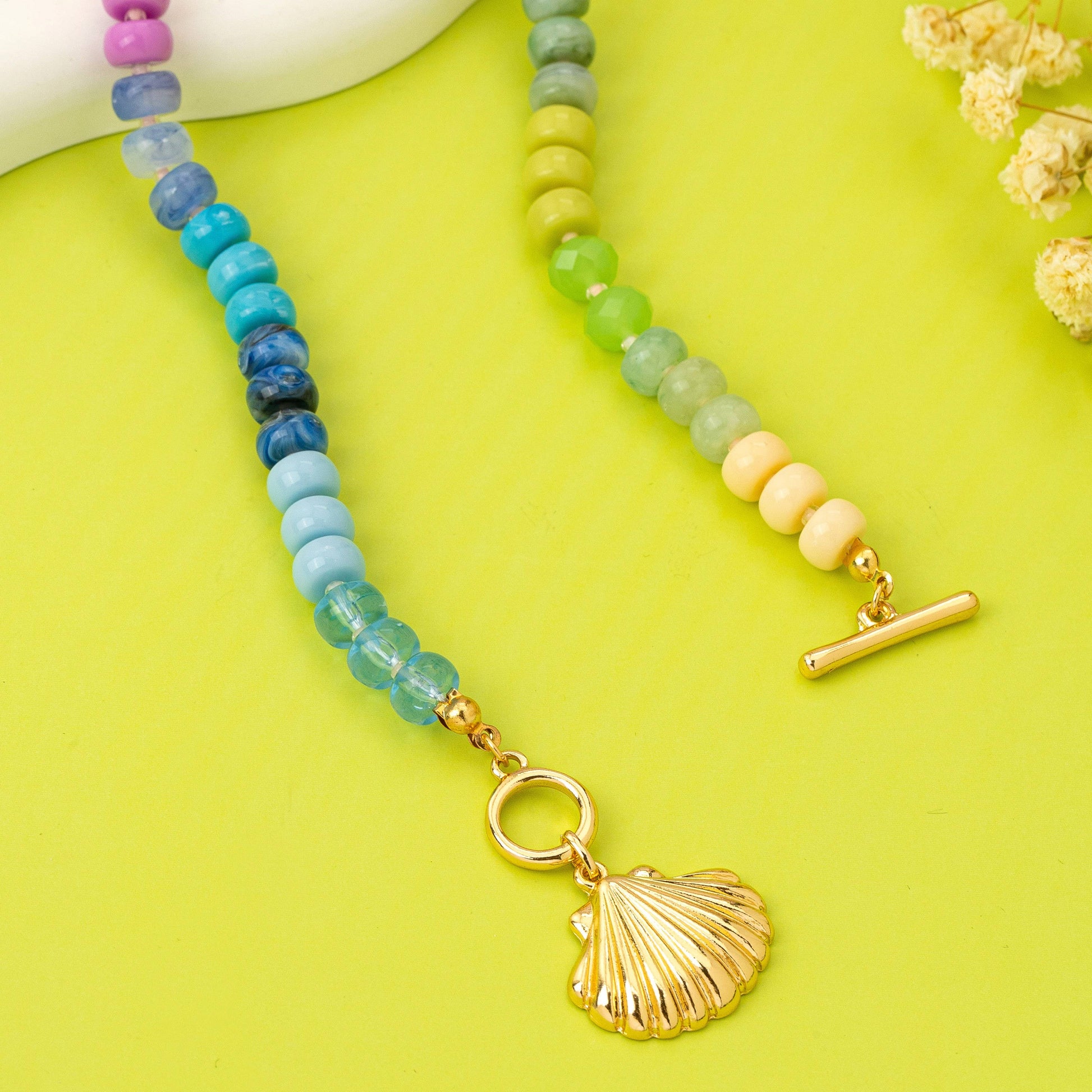 Necklace with colorful beads and a gold shell charm on a yellow background