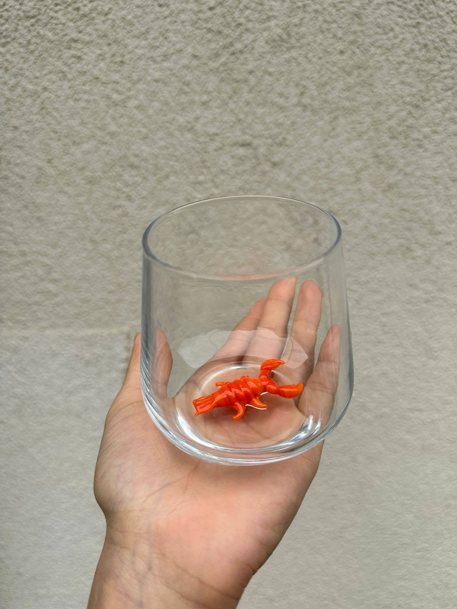 Clear glass container with a small orange object held by a hand against a neutral background