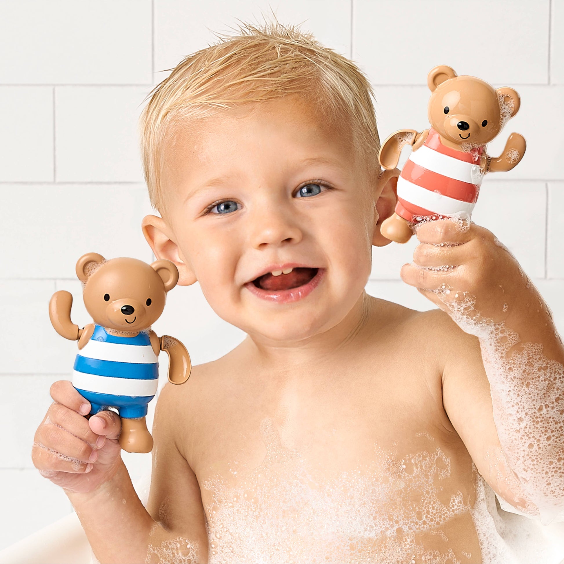 Child in a bath with two teddy bear toys, one held near each ear.