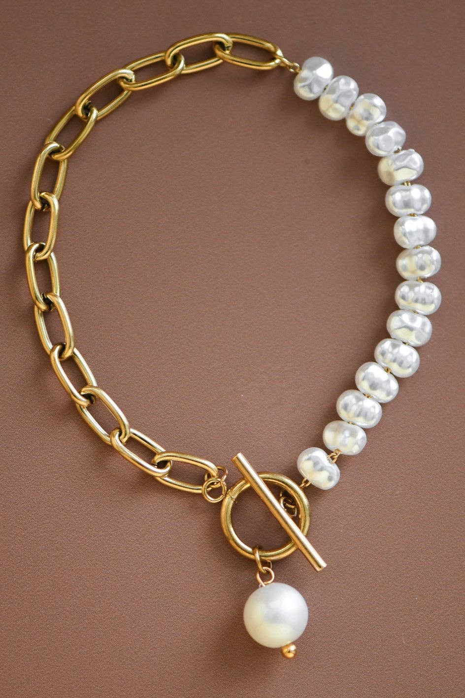 Gold chain bracelet with white pearls on a brown background