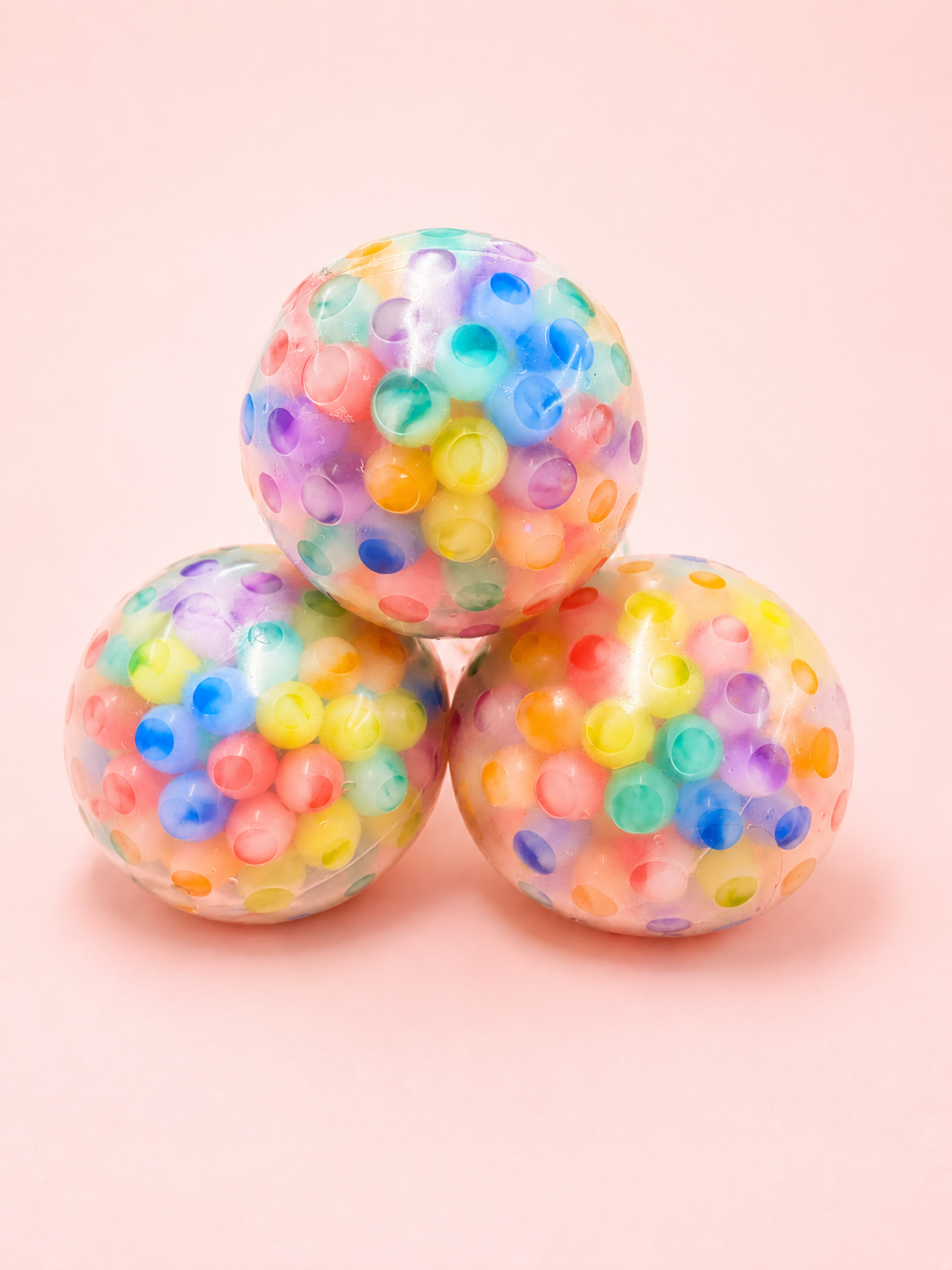 Three colorful spherical objects with multicolored beads on a pink background