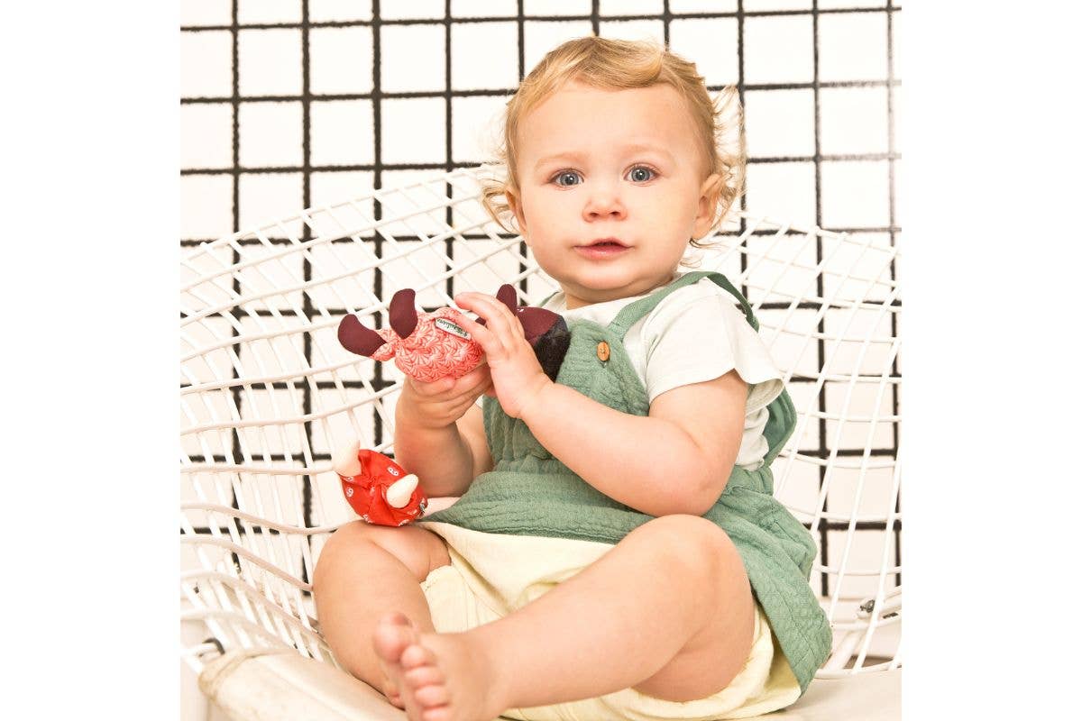 Baby sitting on a white chair holding toys against a black and white checkered background