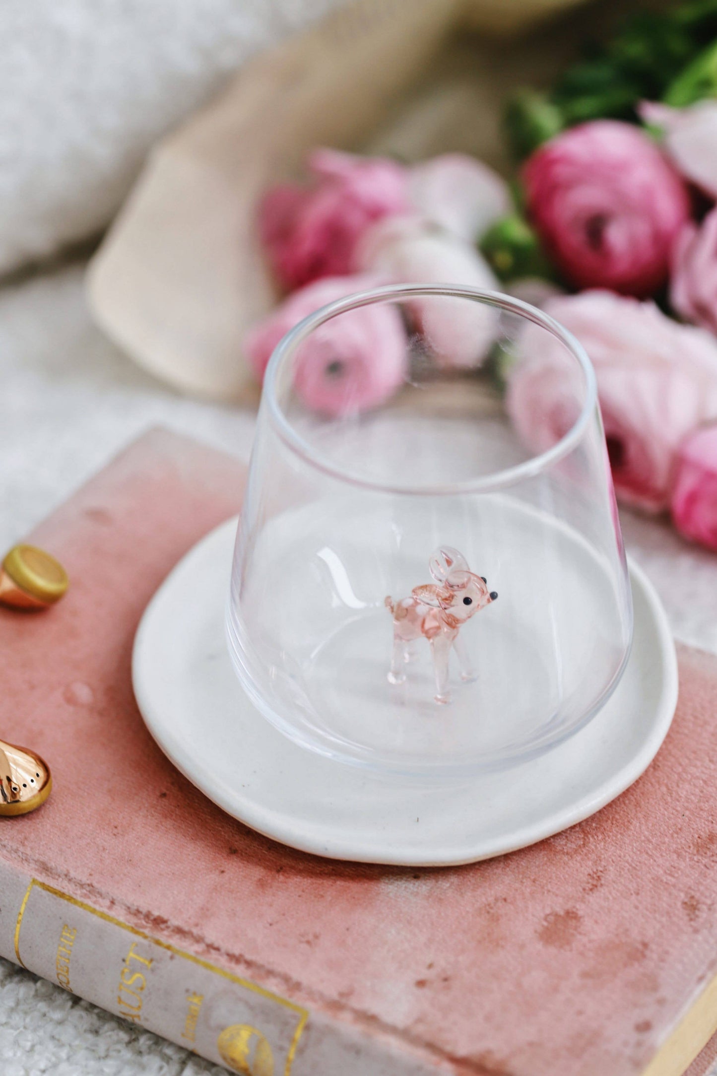 Glass with a deer design on a white coaster on a pink book with flowers in the background