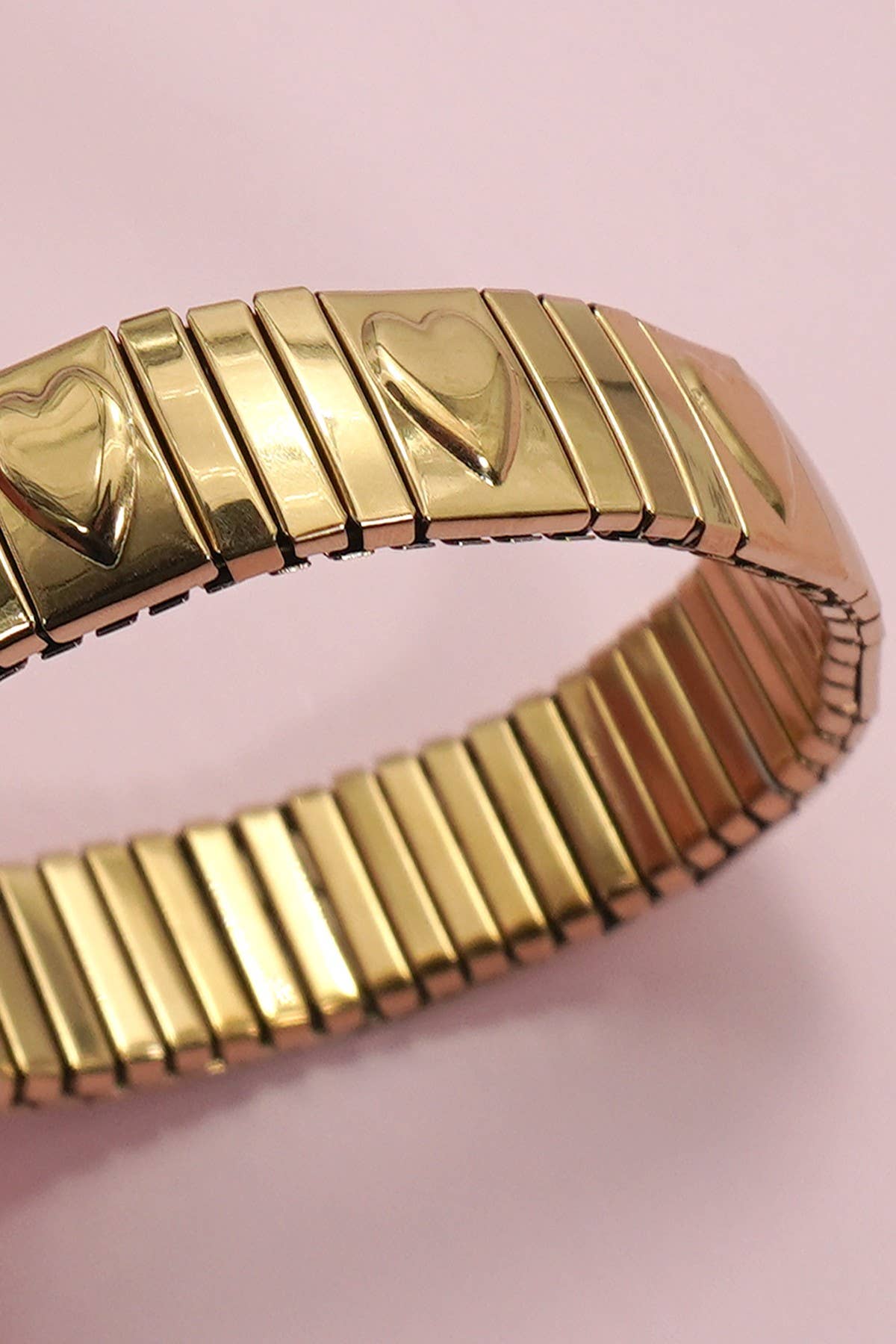 Gold bracelet with heart designs on a pink background