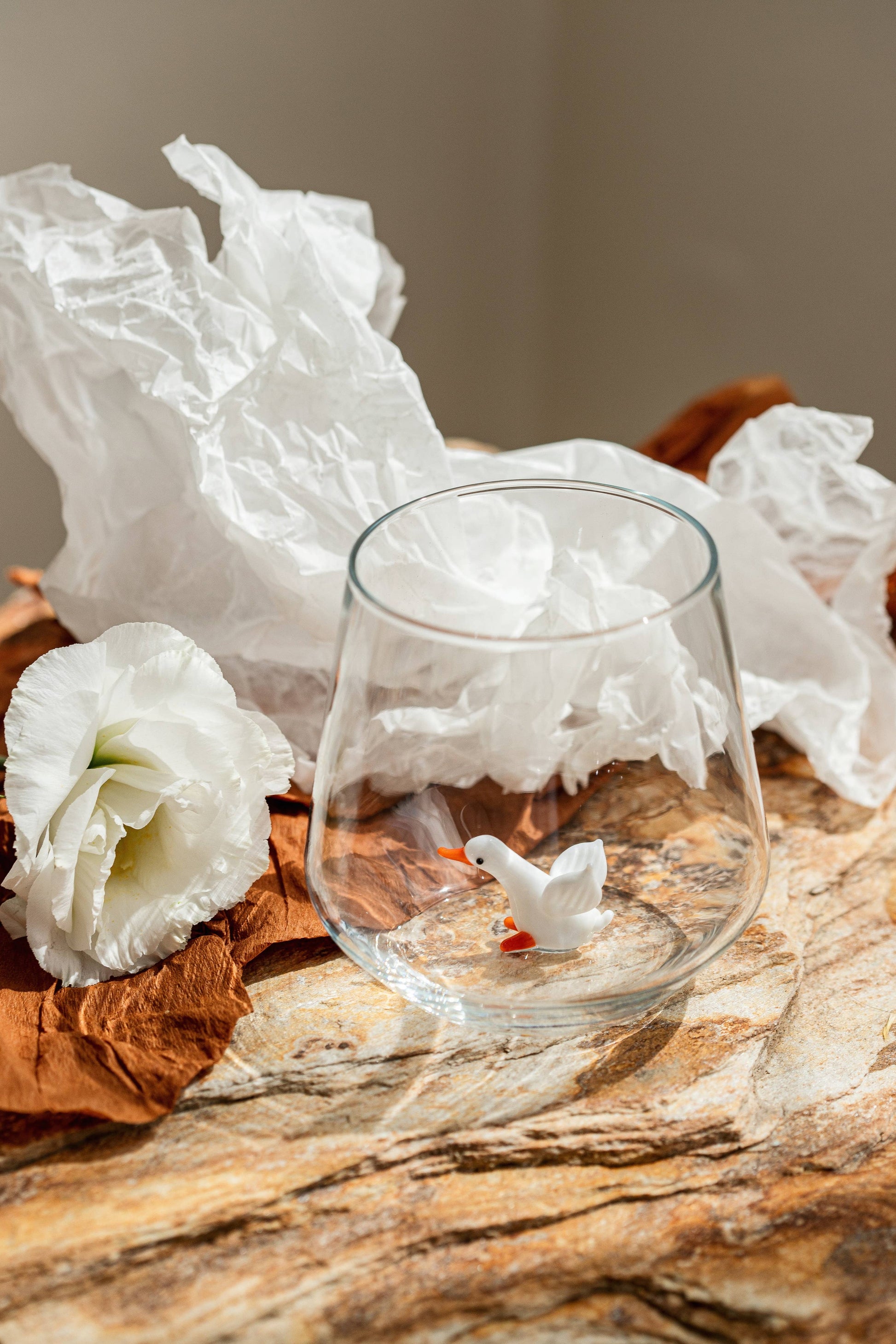 Clear glass with a small figurine on a textured surface with white flowers and brown leaves.