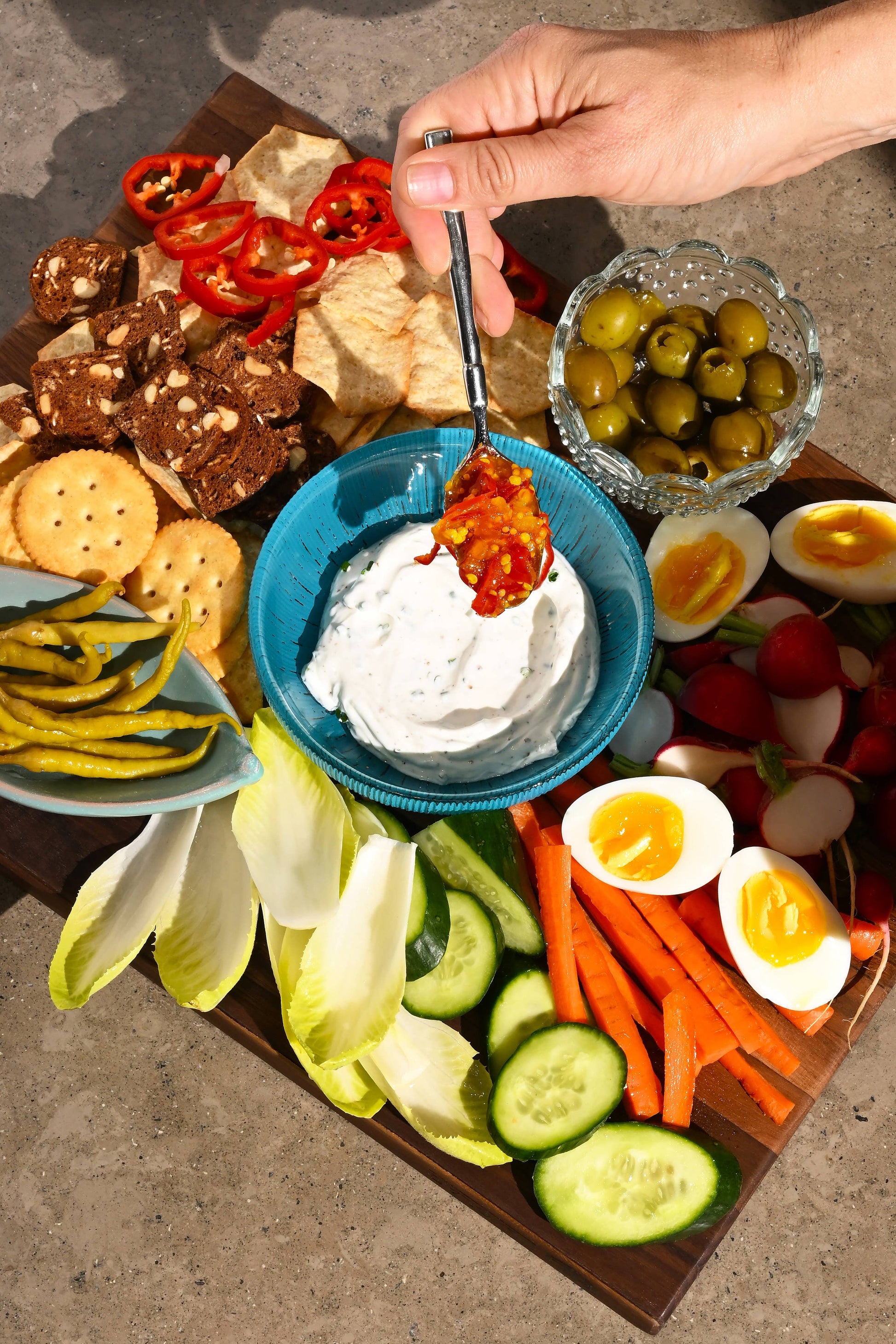 Platter of assorted snacks including crackers, vegetables, and dips on a wooden board.