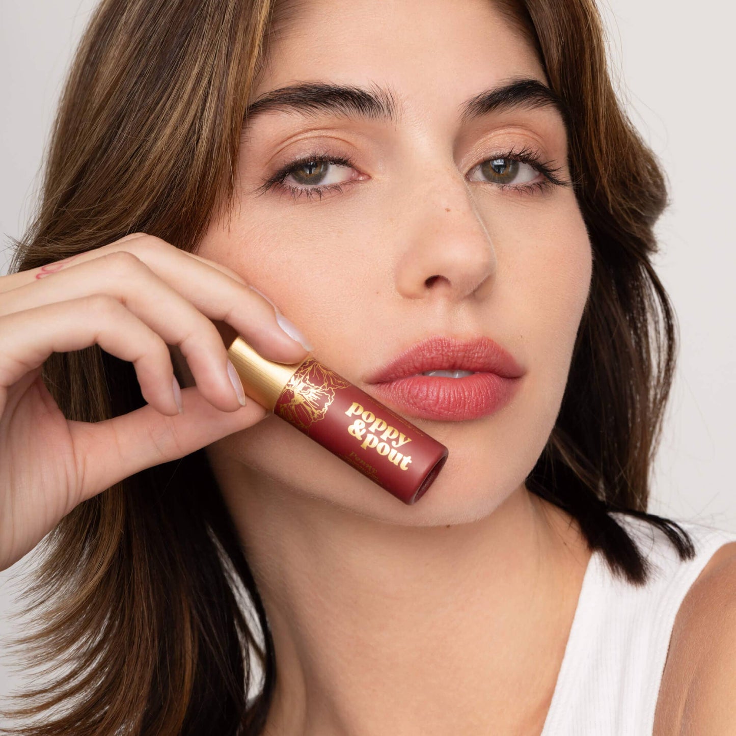 Woman holding a lip balm close to her face with a neutral background