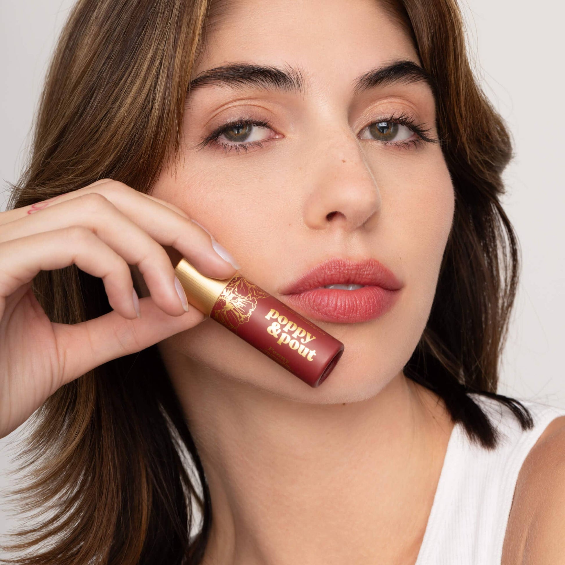 Woman holding a lip balm close to her face with a neutral background