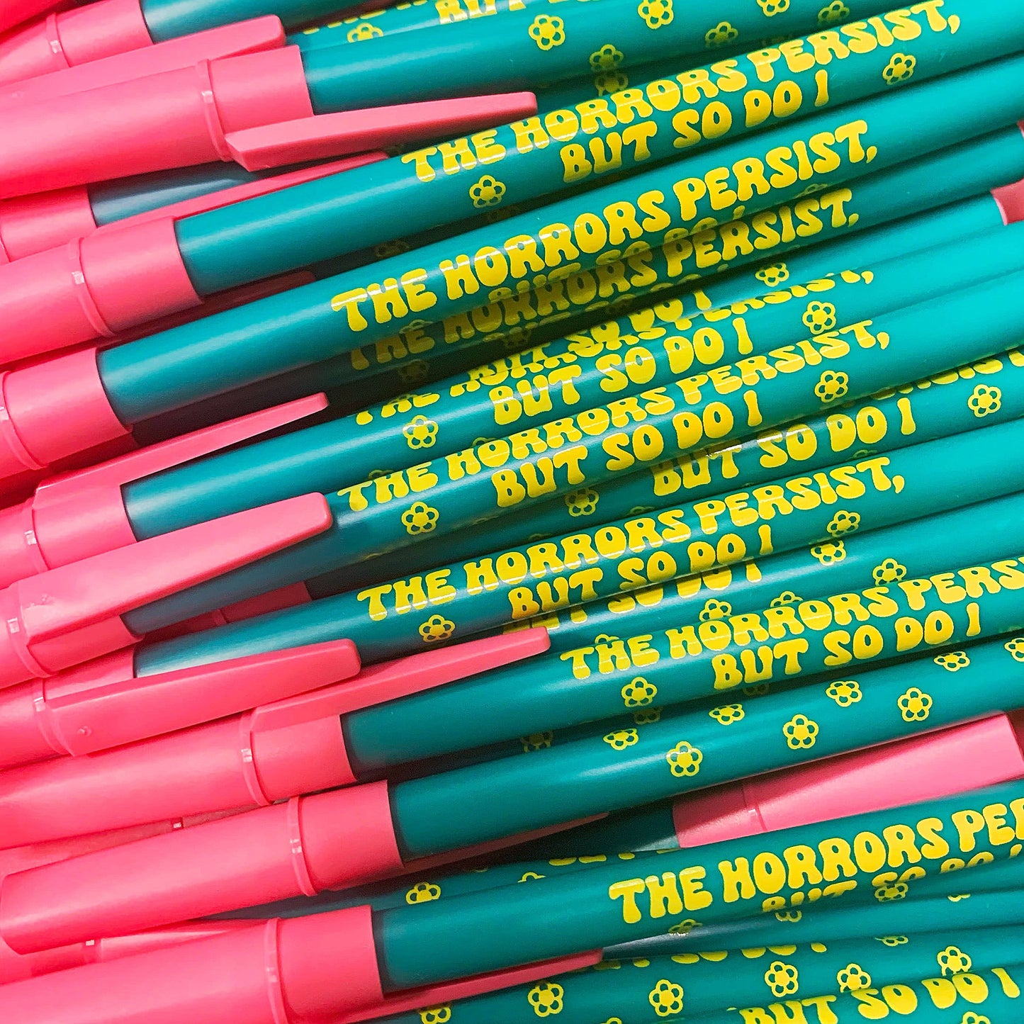 Stack of pens with pink and teal bodies and yellow text.
