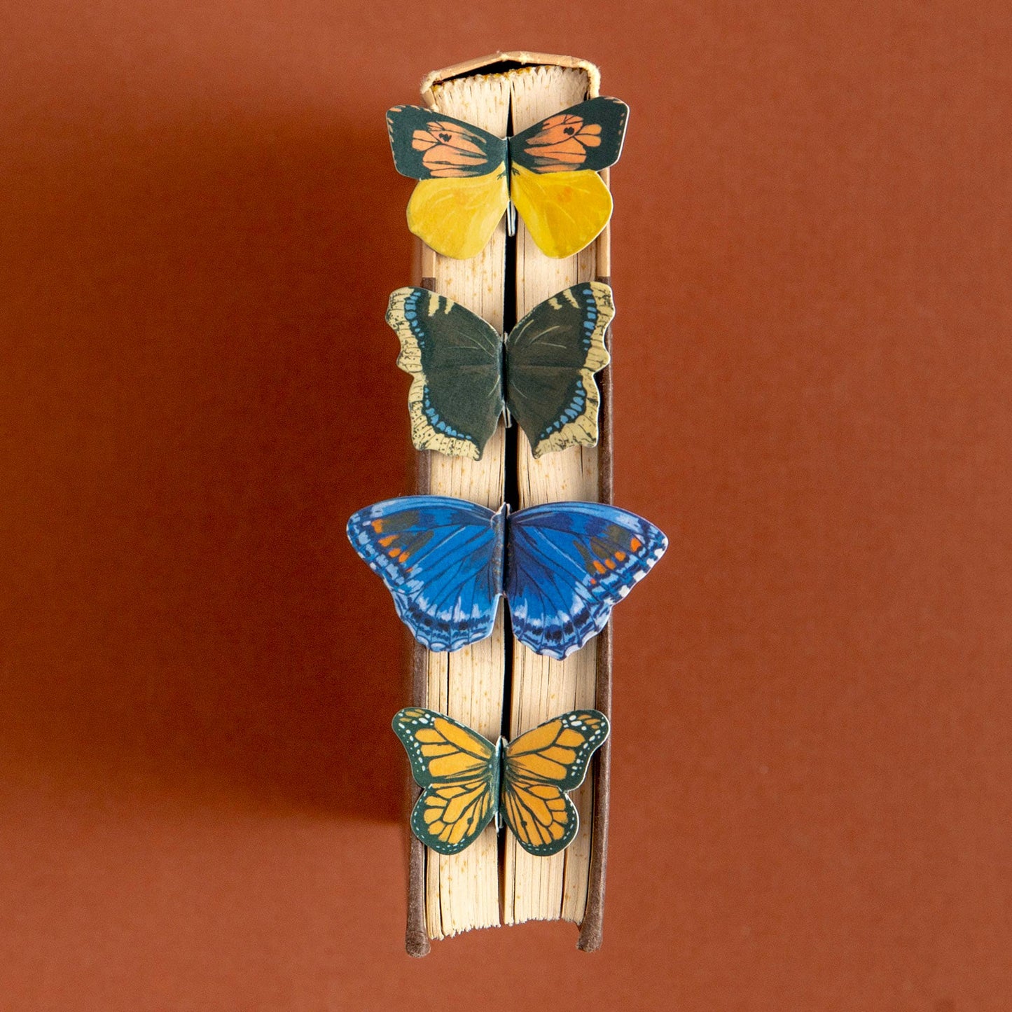 Butterfly-shaped bookmarks on a wooden stick against a brown background