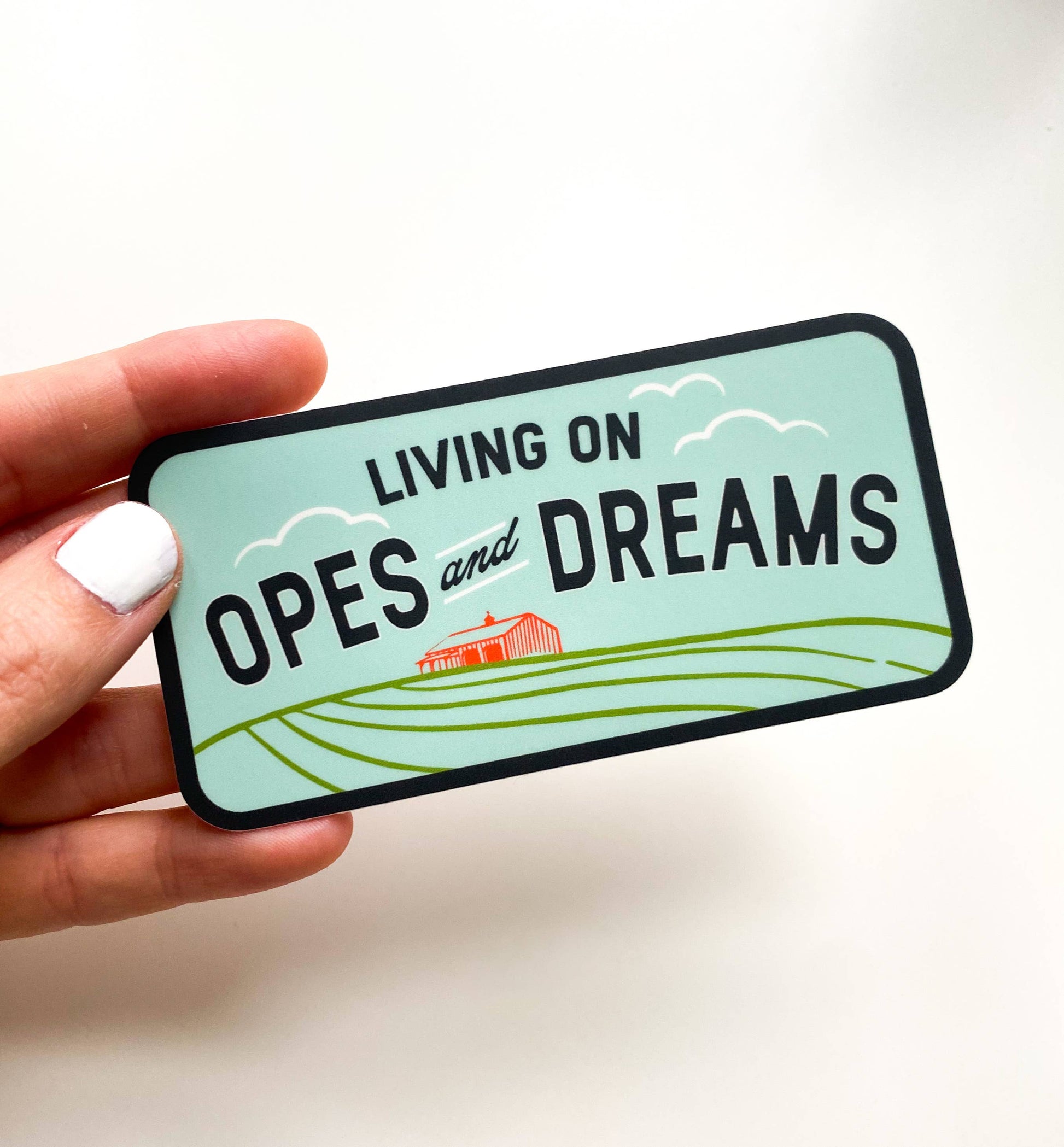 Sticker with 'Living on Opes and Dreams' text held by a hand on a white background