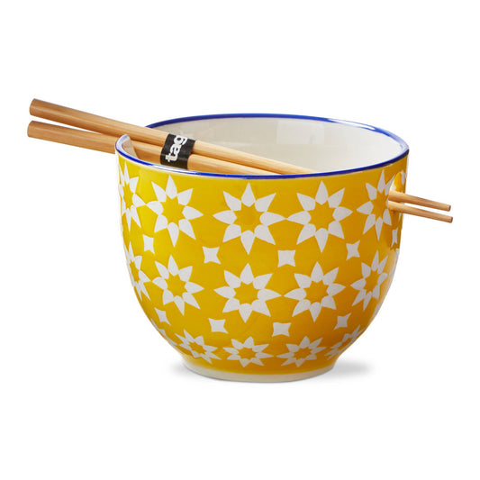A noodle bowl with yellow and white quilted flower design. Blue rim and white interior. Bowl comes with a set of wooden chopsticks which fit into a hole and groove at the top of the bowl. On a white background.