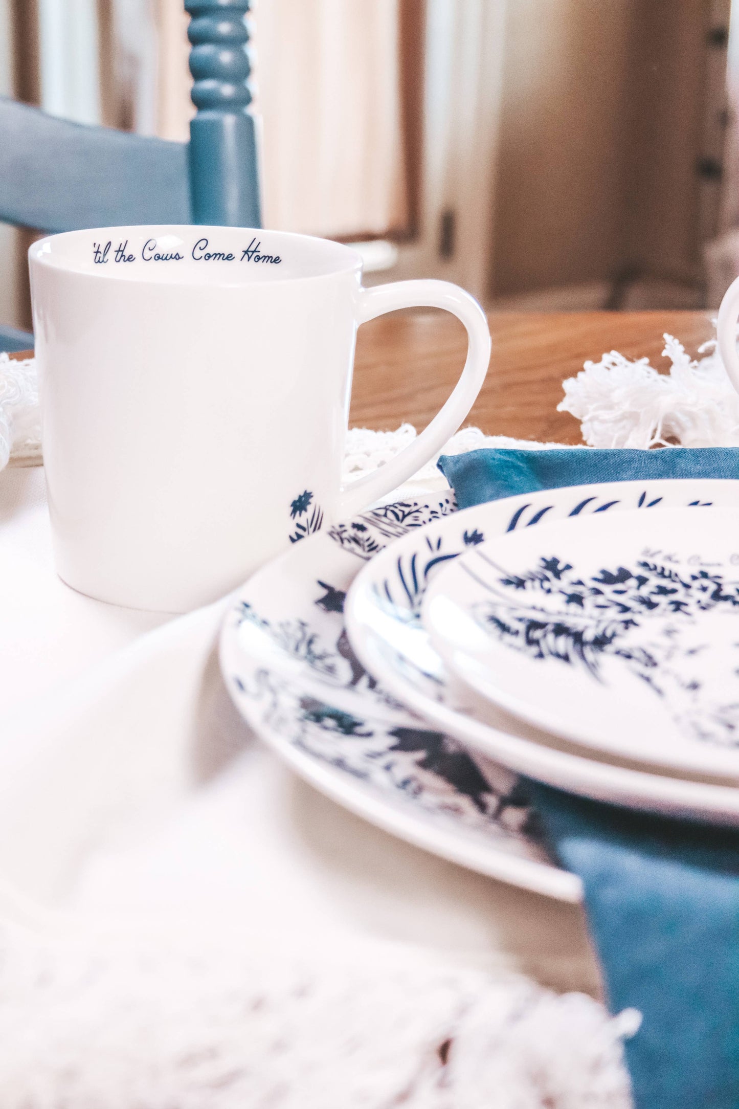 White mug with text on a table with blue and white patterned plates and napkins.