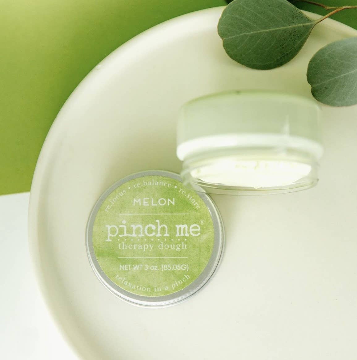 Jar of 'pinch me' therapy dough with a green label on a white surface with a green background