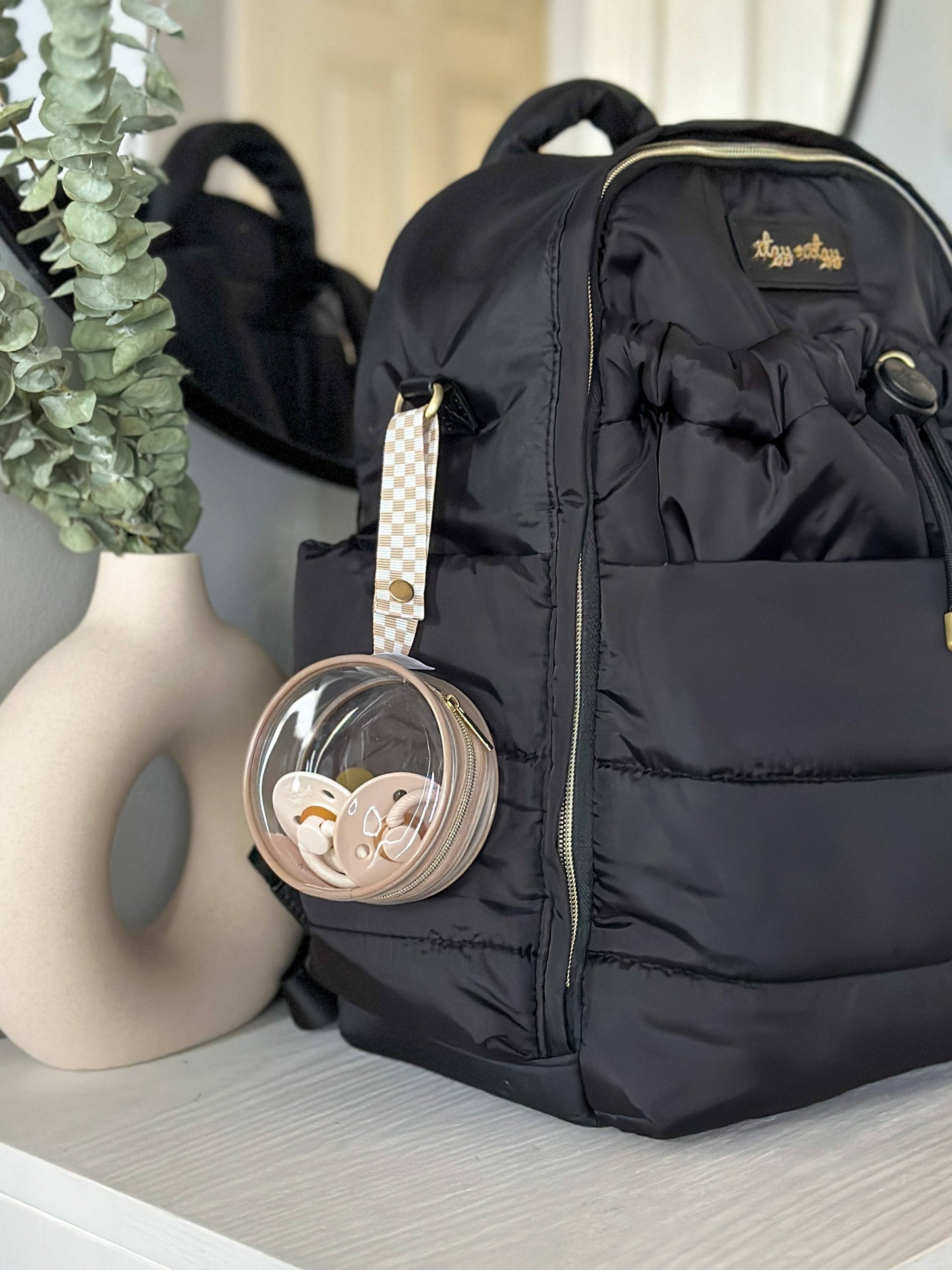Round transparent pacifier holder clipped onto a diaper bag