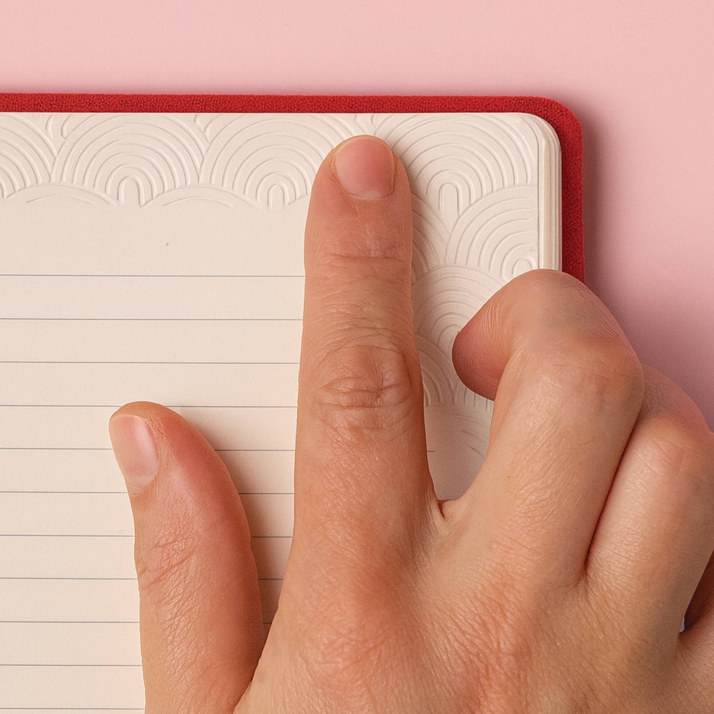 Finger touching notebook paper that is textured with rainbow style pattern etched into pages, showing tactile pages feature of notebook