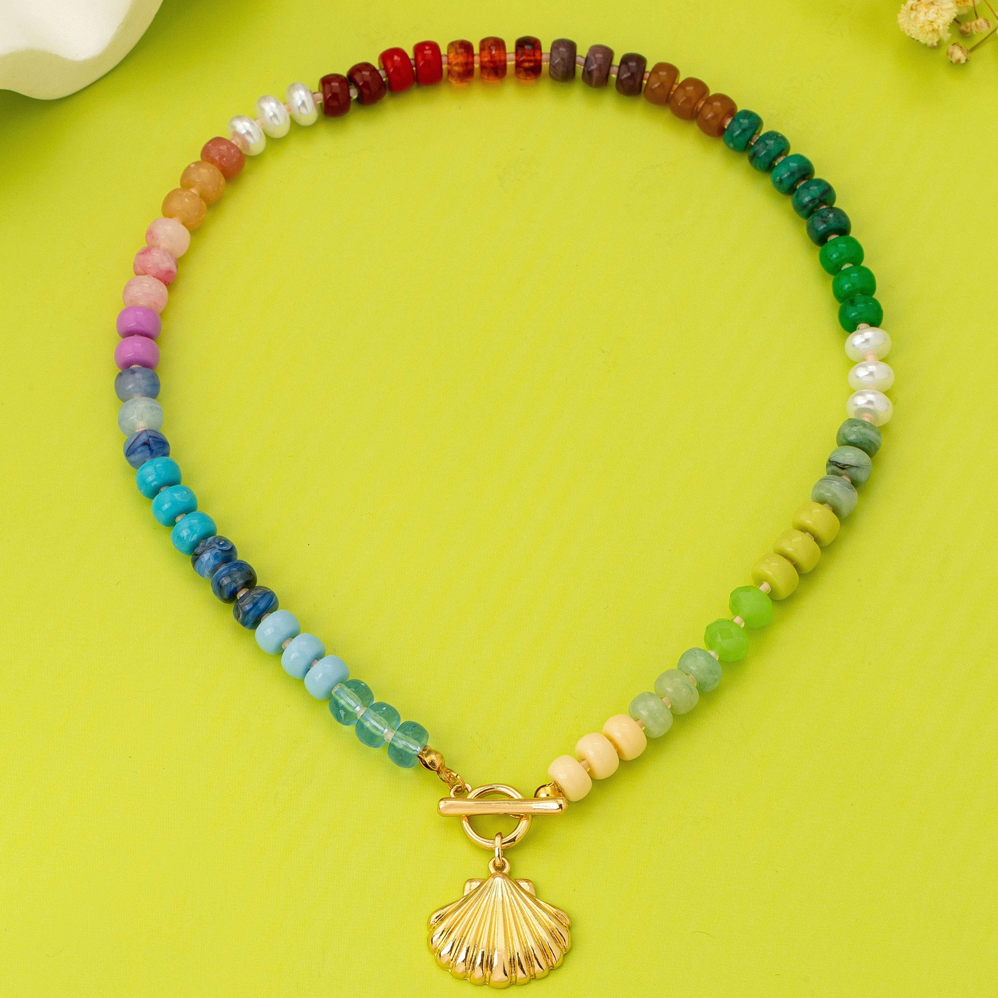 Colorful beaded necklace with a gold shell pendant on a green background