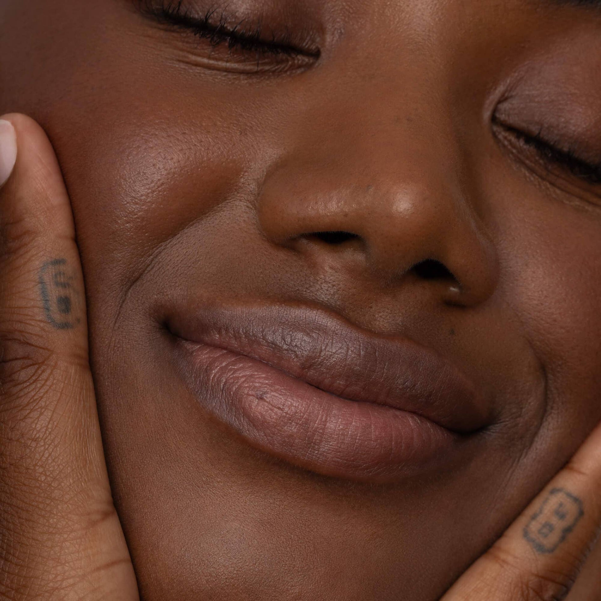 Close-up of a person with tattoos on their fingers touching their face.