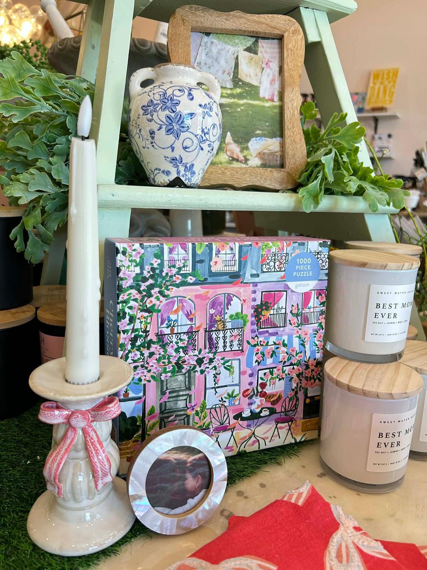Decorative items including a candle, photo frame, and puzzle box on a table with plants in the background.