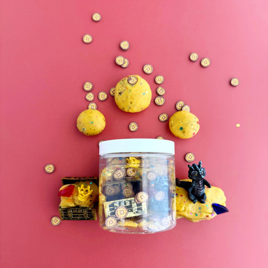 Clear jar with Yellow glittery "kiddough", coin charms, a treasure chest and a dragon figurine inside, on a red background
