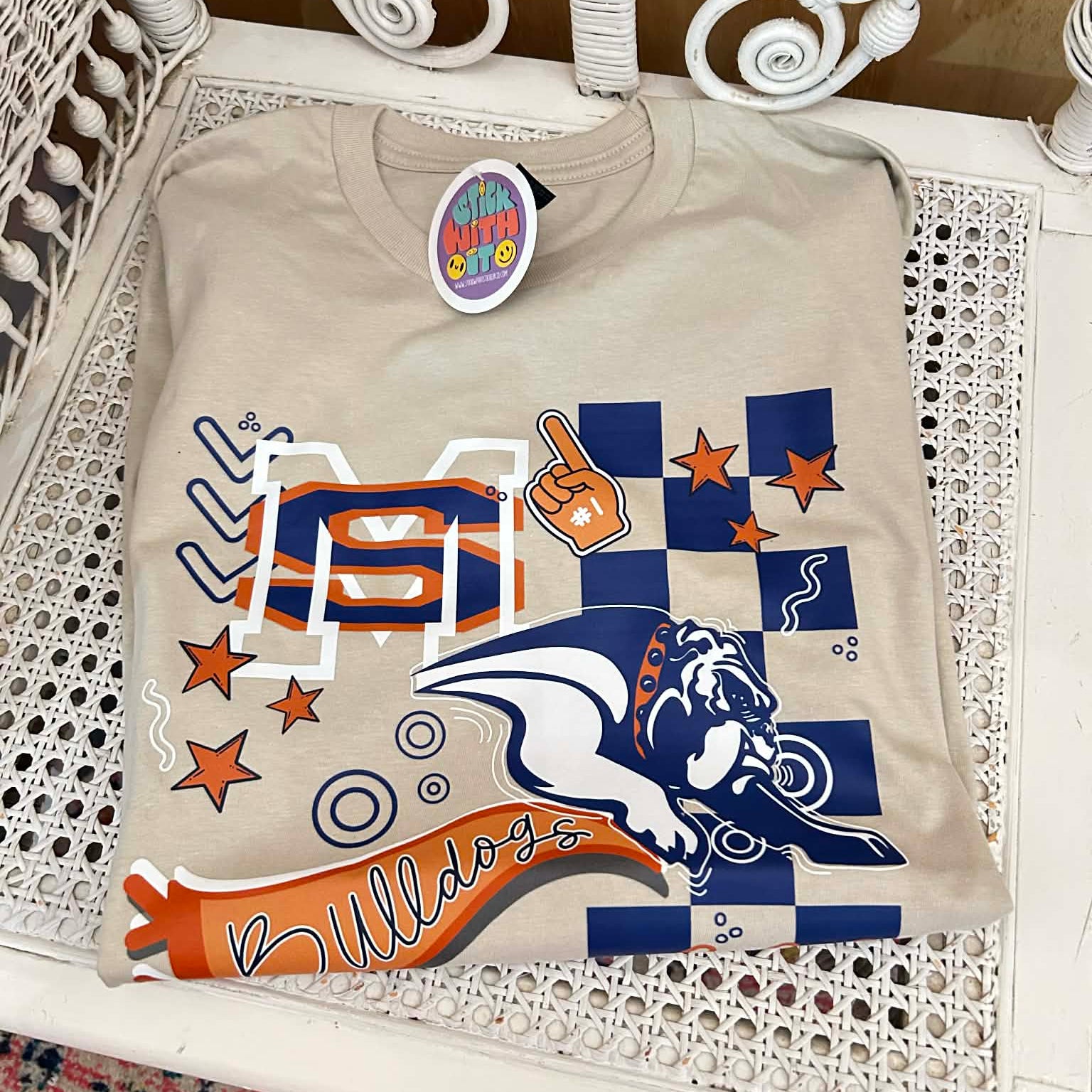 Beige t-shirt with sports team graphics on a white wicker chair