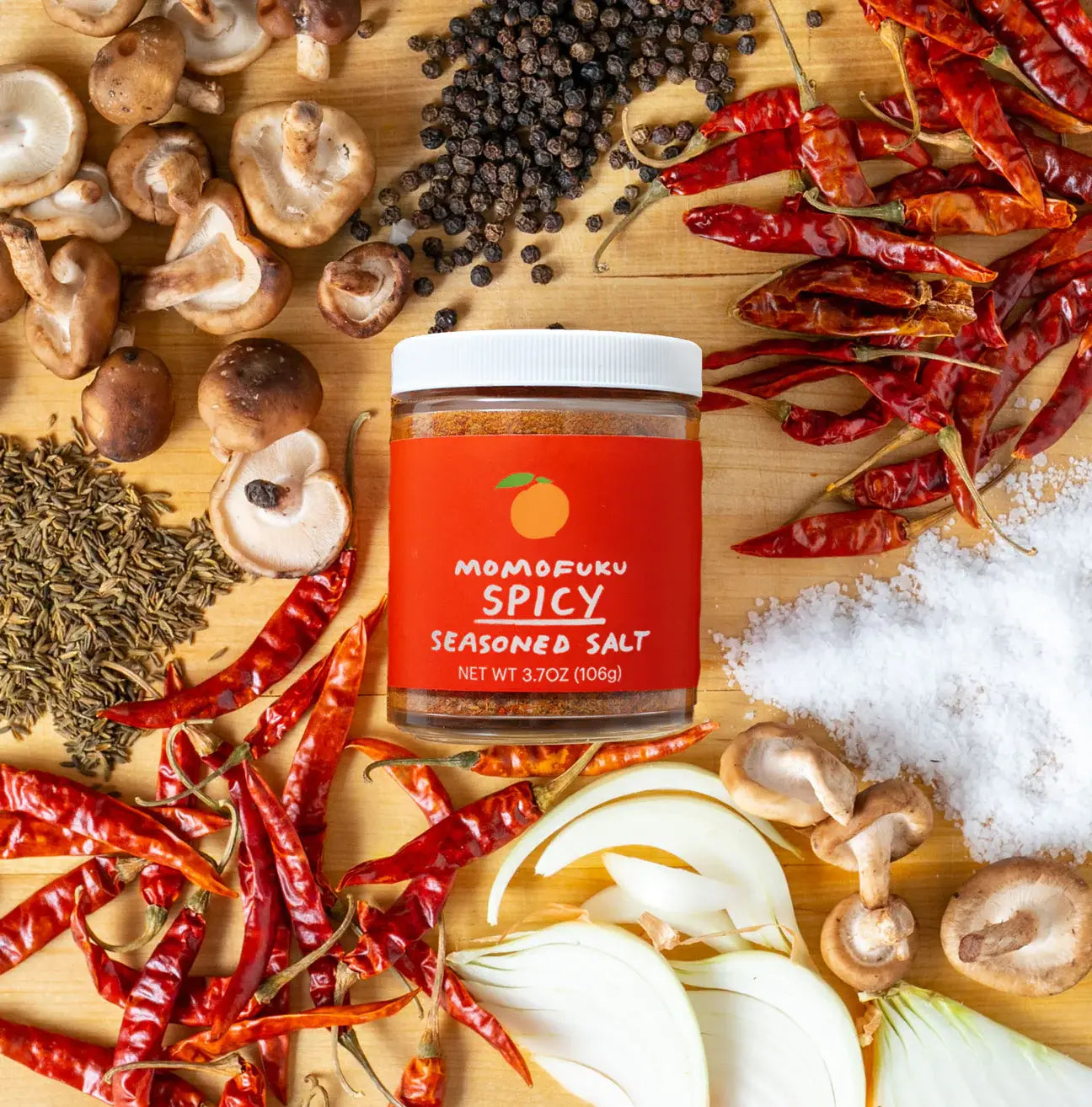 Jar of Momofuku Spicy Seasoned Salt surrounded by spices and herbs on a wooden surface