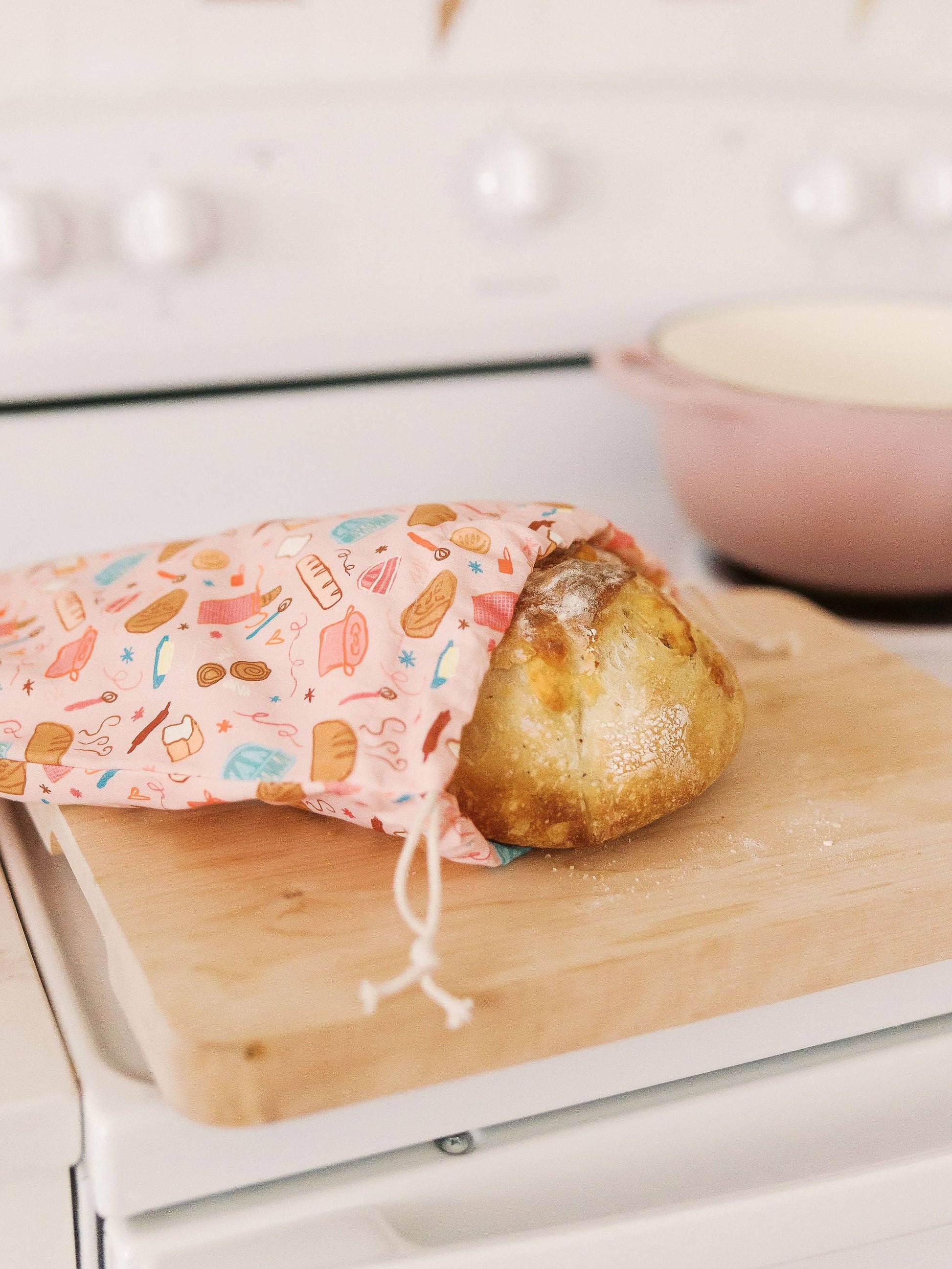 Baked potato on a wooden cutting board with a colorful cloth over it, placed on a stove.