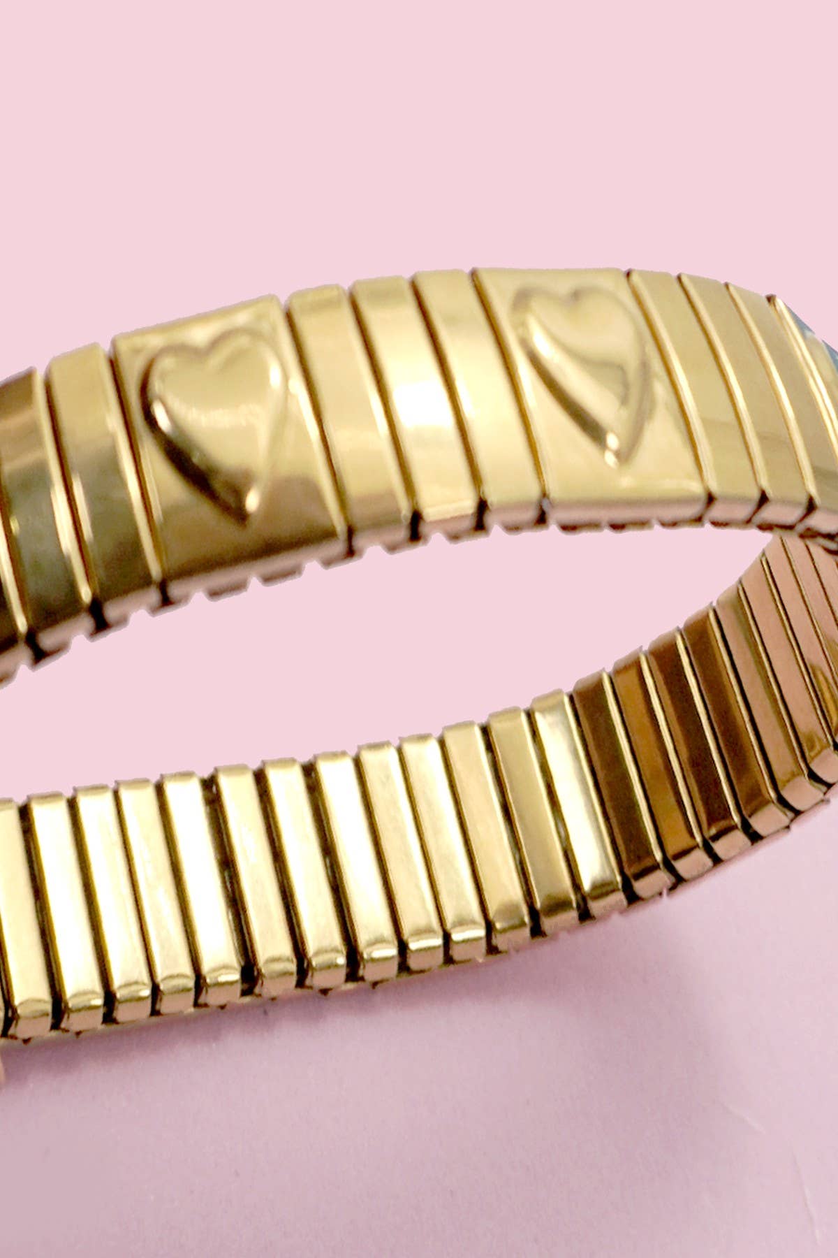 Gold bracelet with heart designs on a pink background