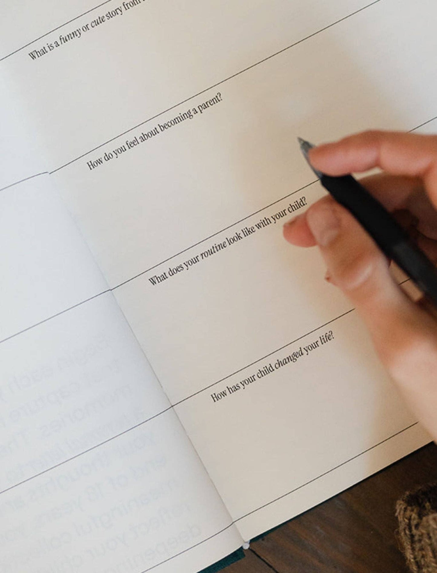Hand holding a pen over a notebook with writing prompts on a wooden surface