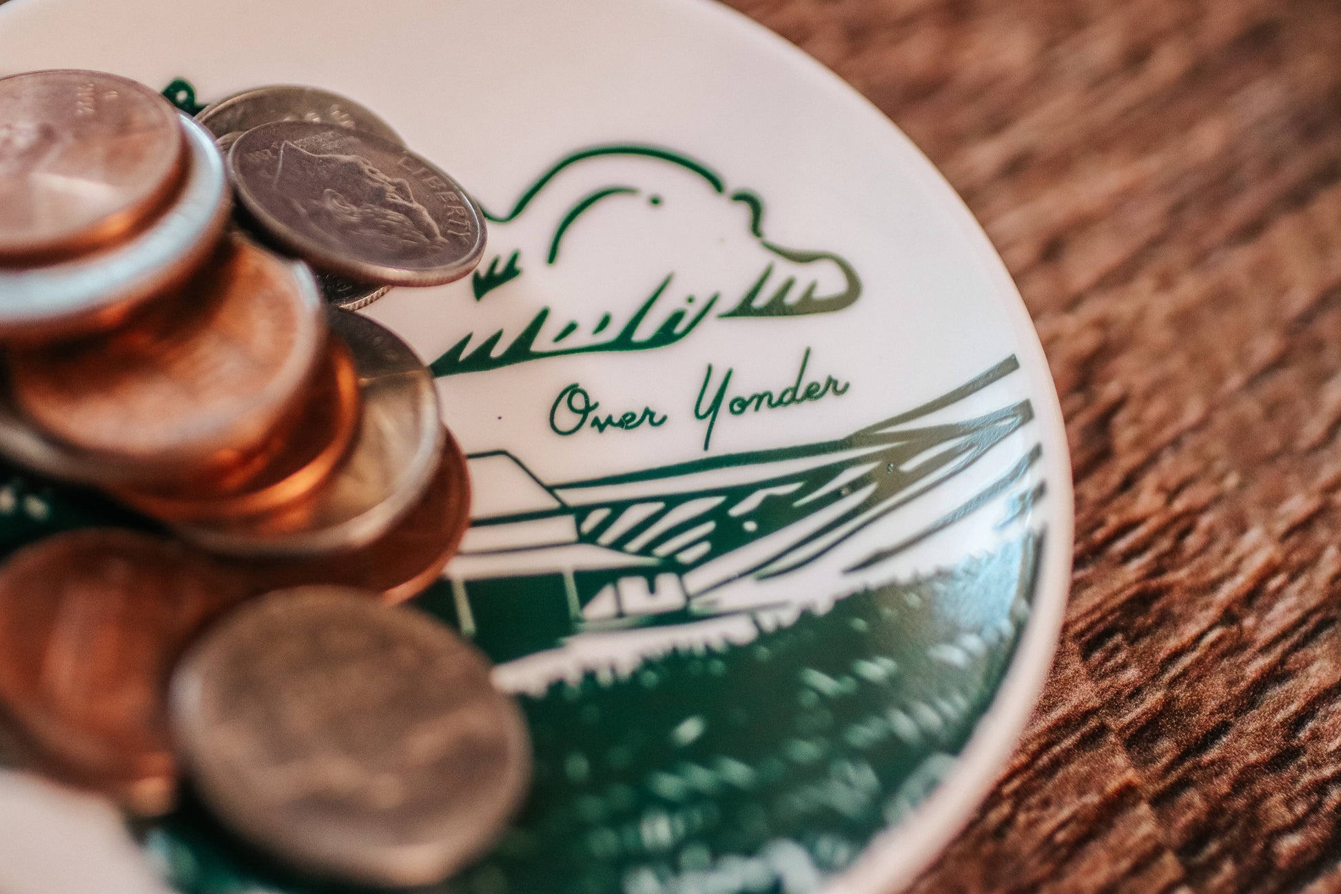 Close-up of coins on a ceramic butter pat with a scenic design and text.