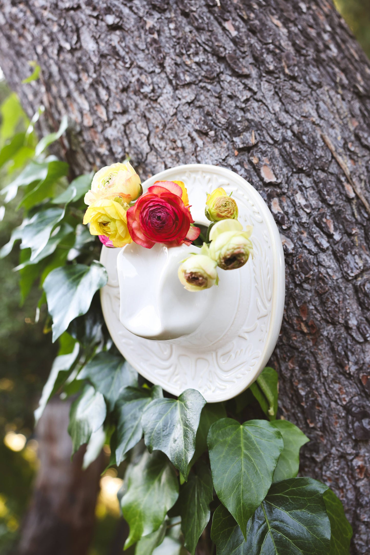White ceramic Cowboy hat shaped vase with decorative patterns hanging on a tree