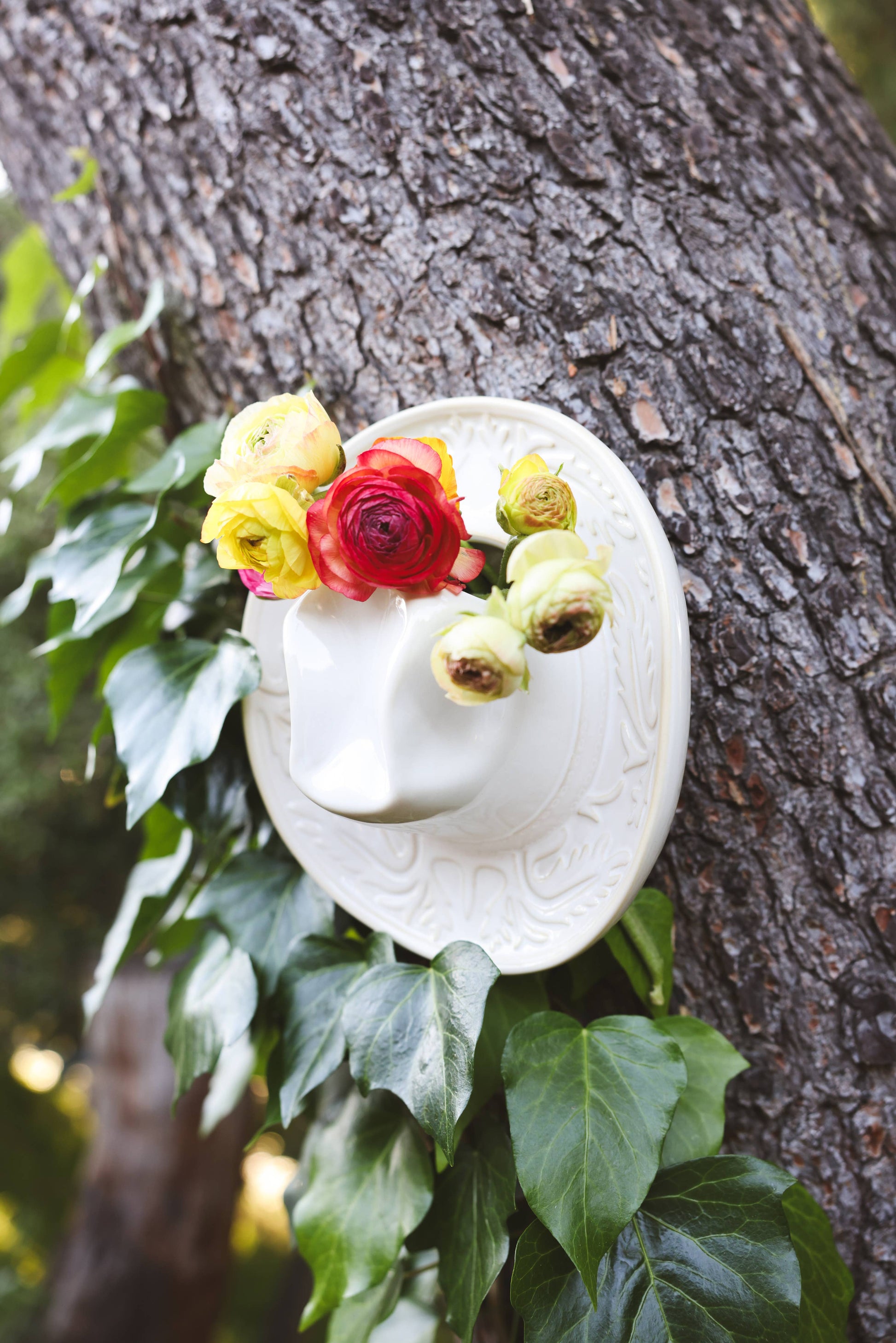 White ceramic Cowboy hat shaped vase with decorative patterns hanging on a tree