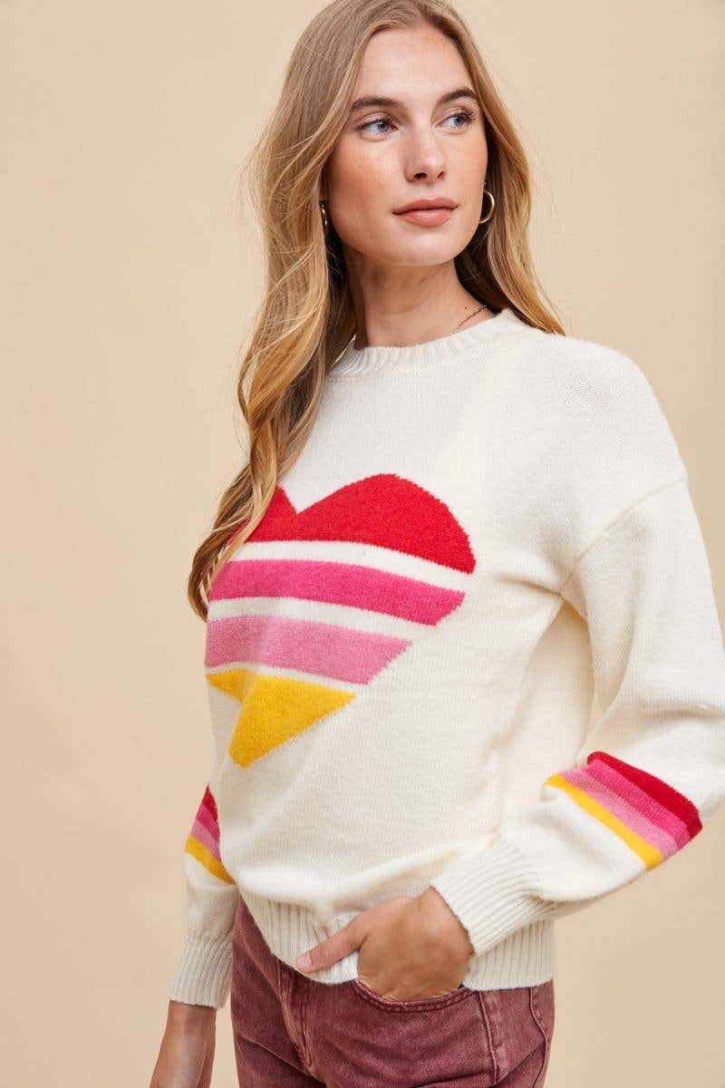 Side view of a woman wearing an ivory sweater with heart motif in the center made of 4 red, hot pink, light pink, and yellow stripes, and stripes of the same colors around the sleeves