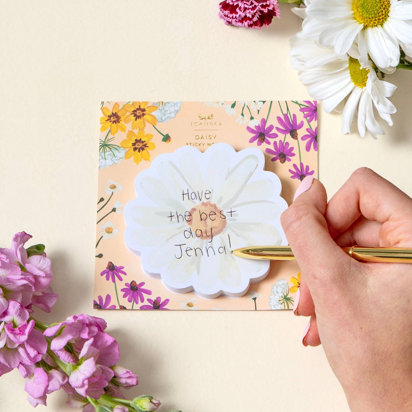 Hand writing on a flower-shaped sticky note with a floral card in the background