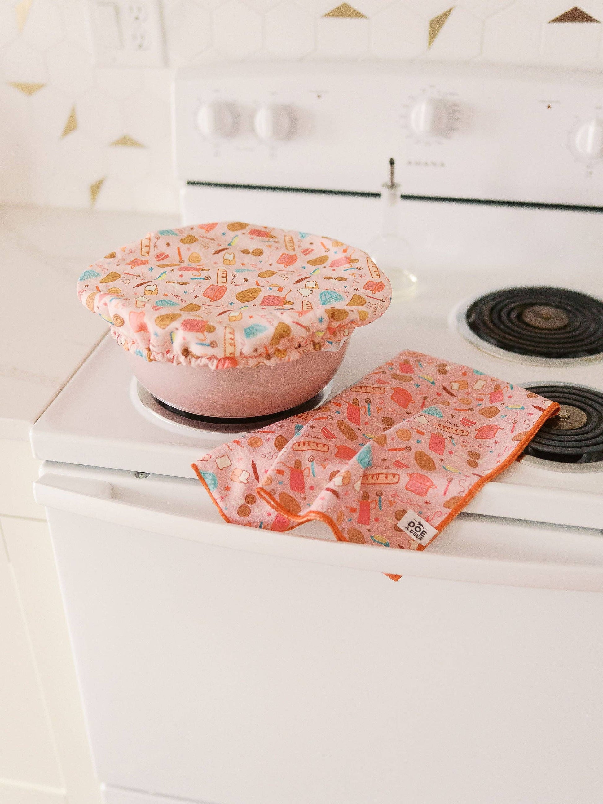 Pink pot holder and matching dish cover on a white stove