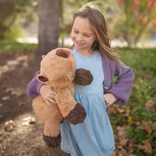 Young girl holding a large brown teddy bear outdoors.