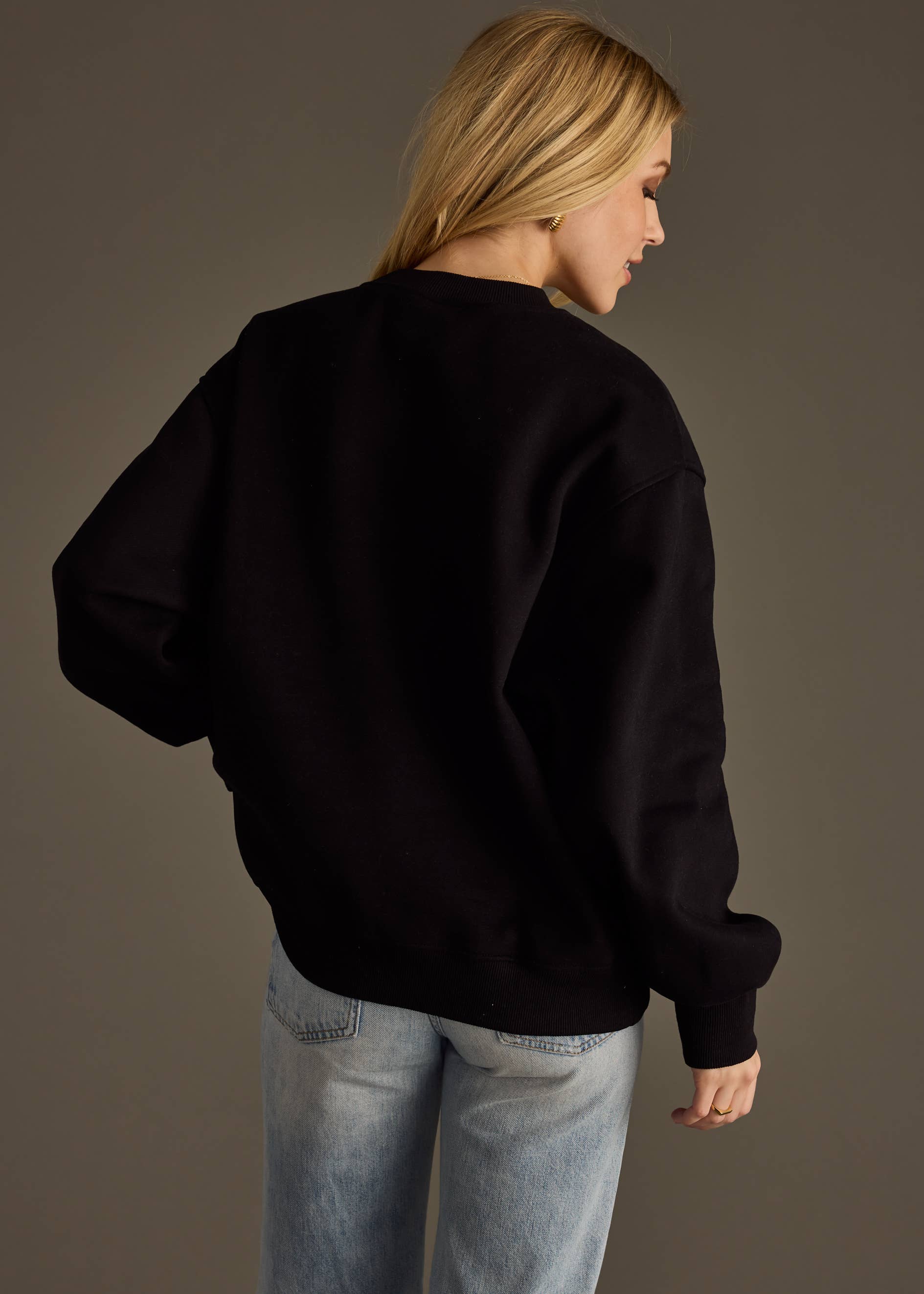 Back view of a woman wearing a black sweatshirt on a plain background