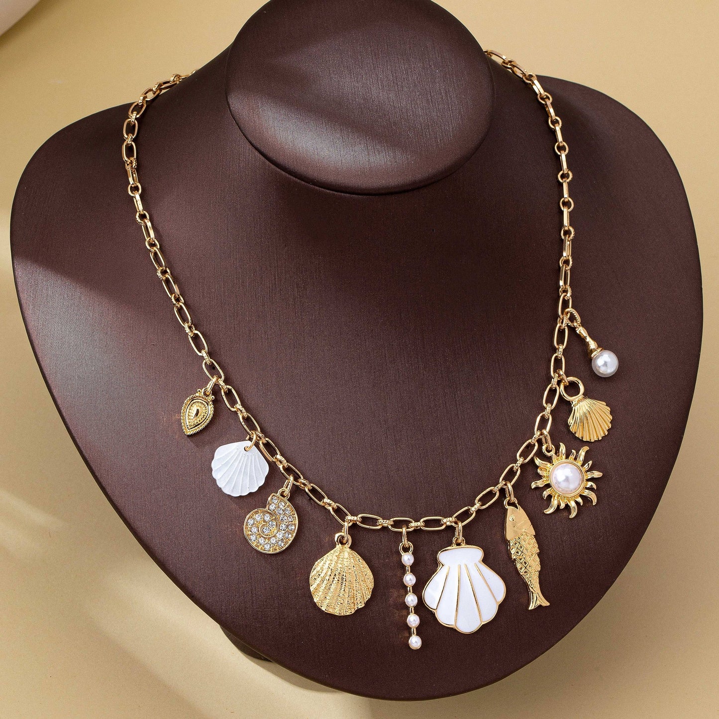 Gold necklace with various charms on a brown mannequin head against a beige background